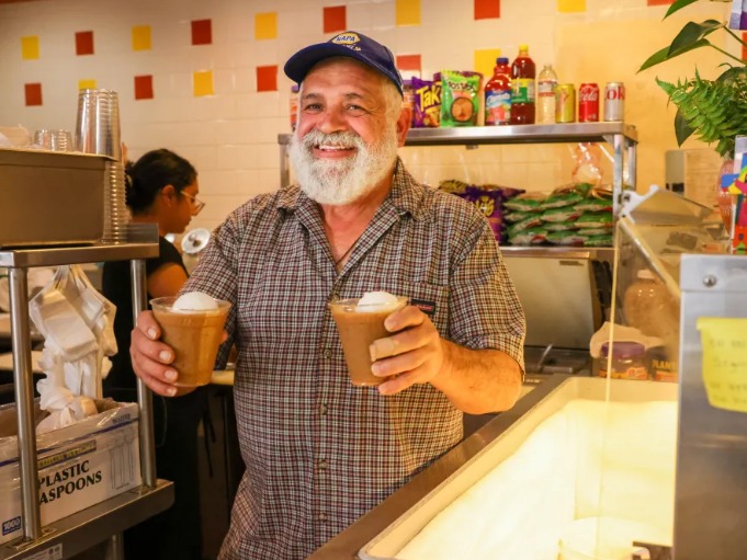 A local merchant smiling and holding two horchatas
